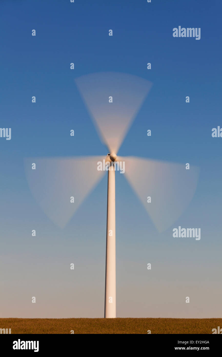 Spinning blades of windt urbine in field against blue sky Stock Photo