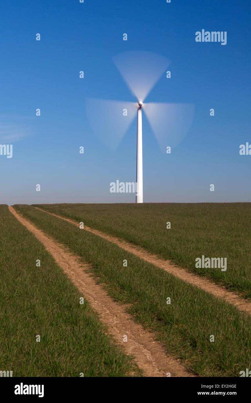 Spinning blades of wind turbine in field against blue sky Stock Photo