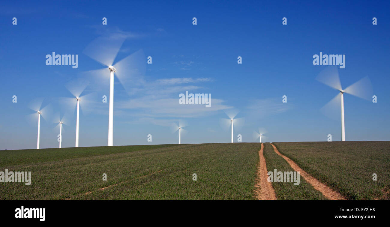 Spinning blades of wind turbines at wind farm against blue sky Stock Photo