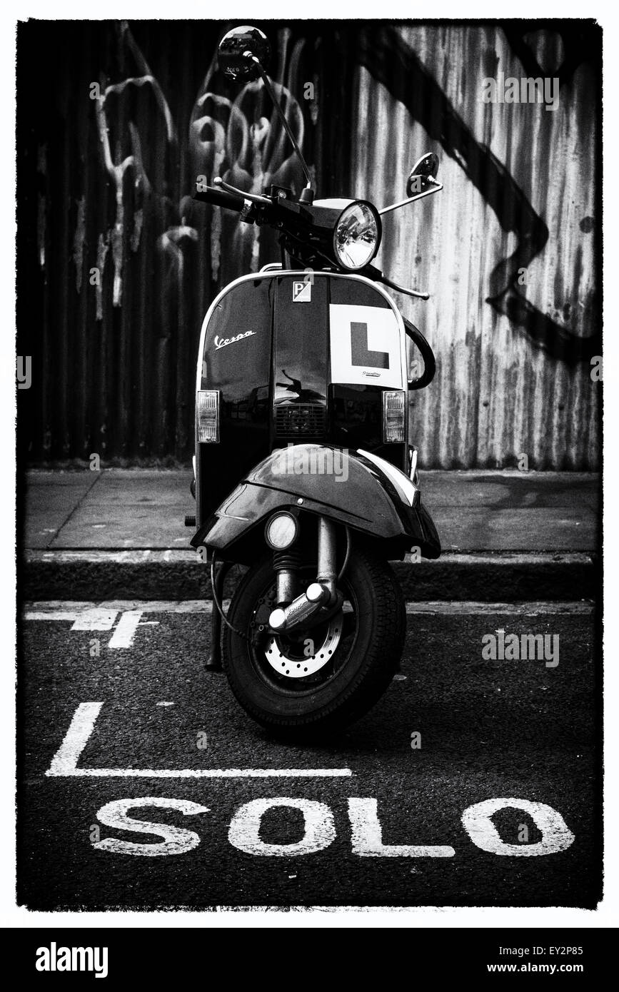 A Vespa scooter parked in a motorcycle bay with the word 'solo' marked on the road infront of it Stock Photo