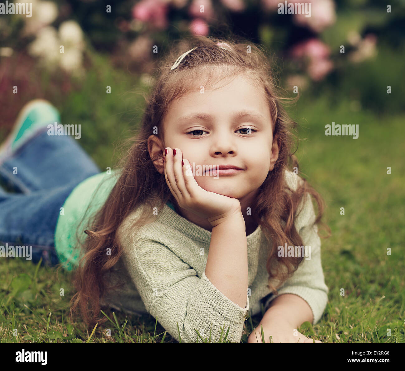 Beautiful Long Curly Hair Kid Girl Lying On Green Grass In Fashion