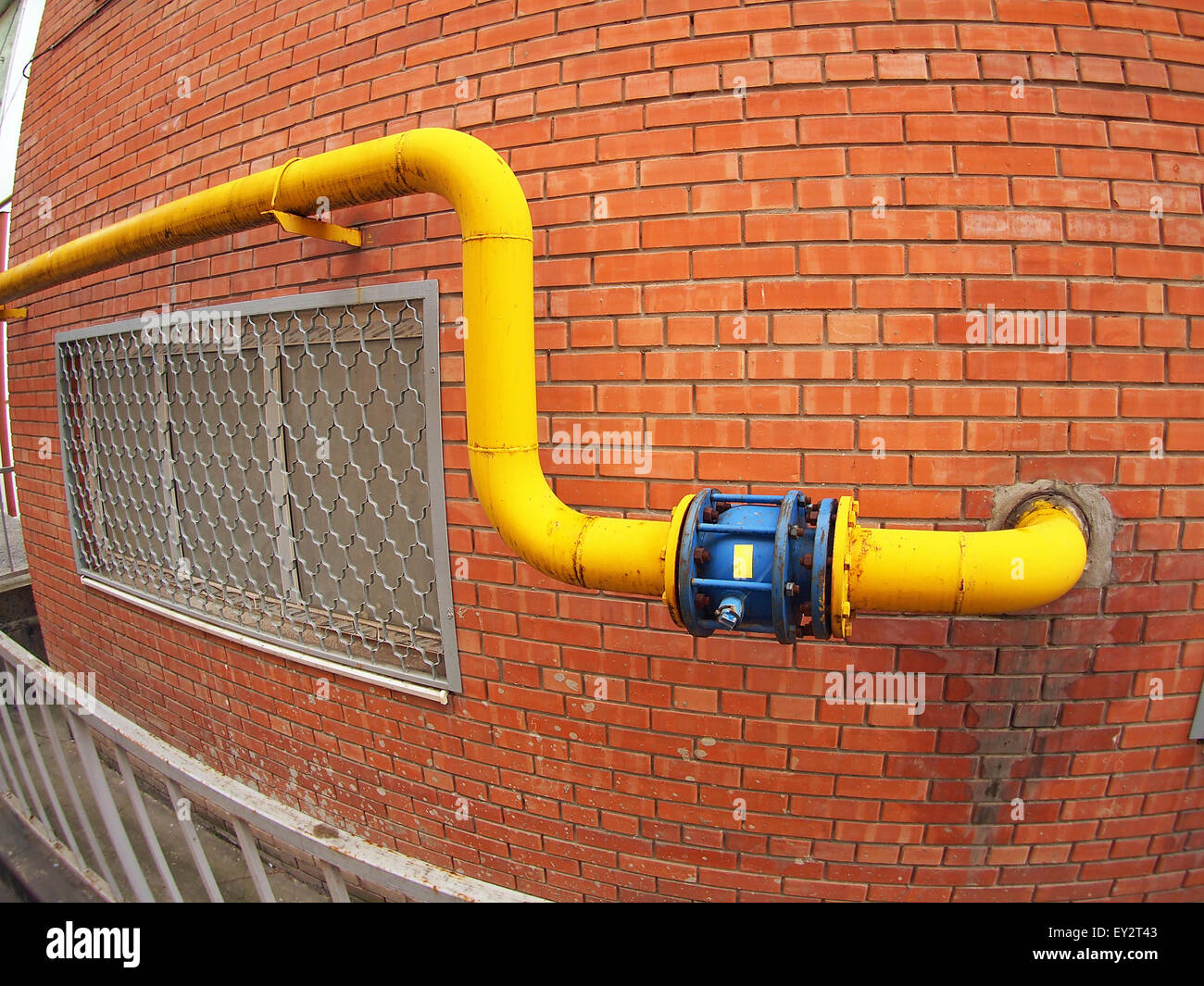 Wall of a building with a yellow gas pipe and a large valve with wide angle fisheye view Stock Photo