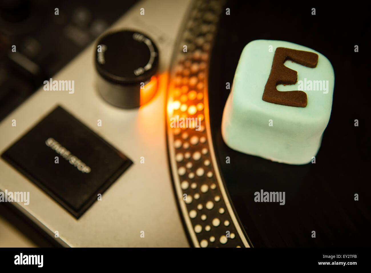 A cake with E for ecstasy written on it sitting on a Dj's record deck Stock Photo