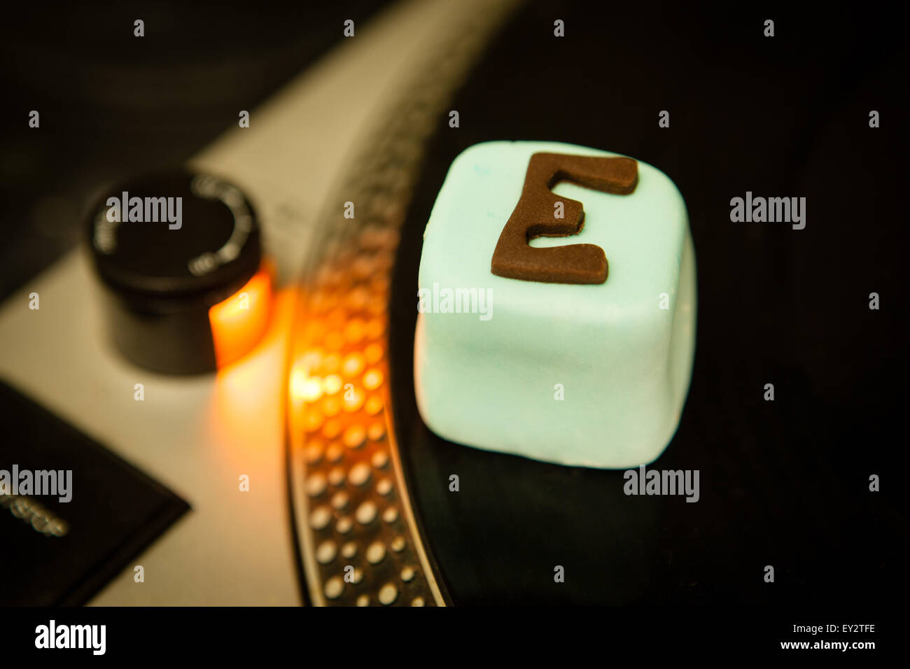 A cake with E for ecstasy written on it sitting on a Dj's record deck Stock Photo