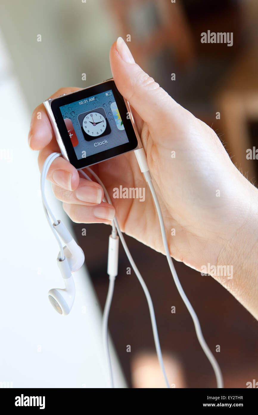Close up of an Apple iPod nano, with headphones, held in a womans hand showing the Clock screen. Stock Photo