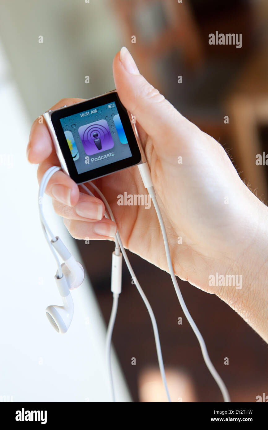 Close up of an Apple iPod nano, with headphones, held in a womans hand showing the podcasts screen. Stock Photo