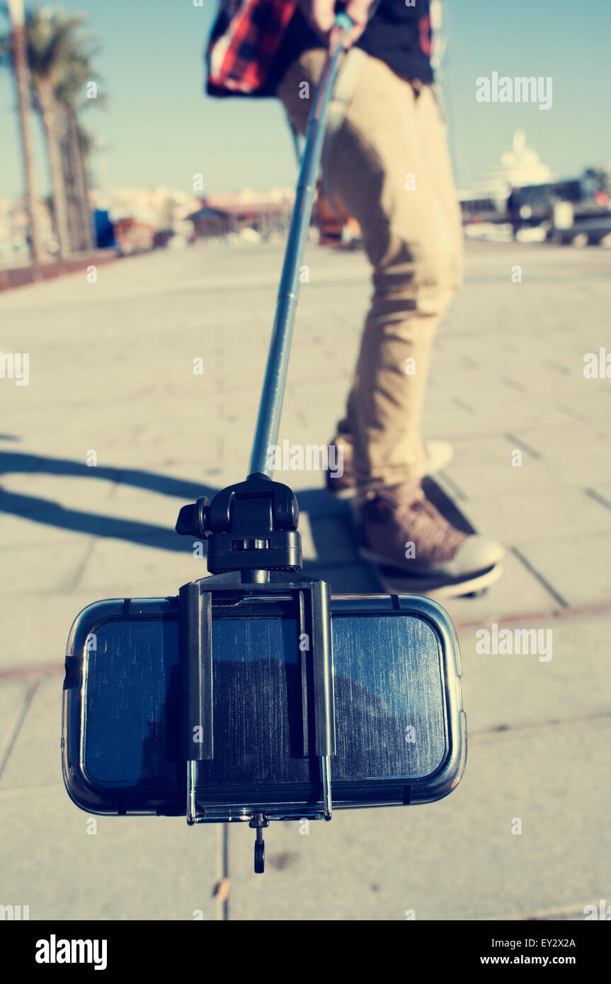 a young skater on his skateboard takes a self-portrait or a video of himself with a selfie stick Stock Photo