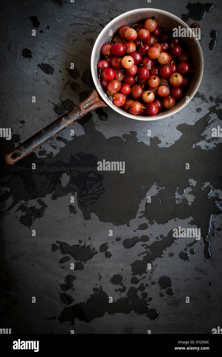 Vintage colander with gooseberries over wet slate background. Top view ...