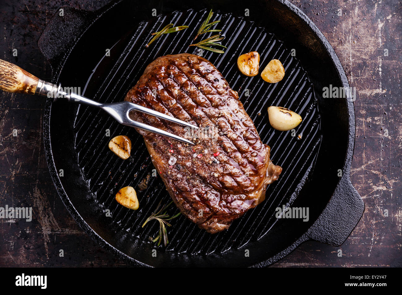 Grilled Ribeye steak and meat fork on grill iron pan on dark background