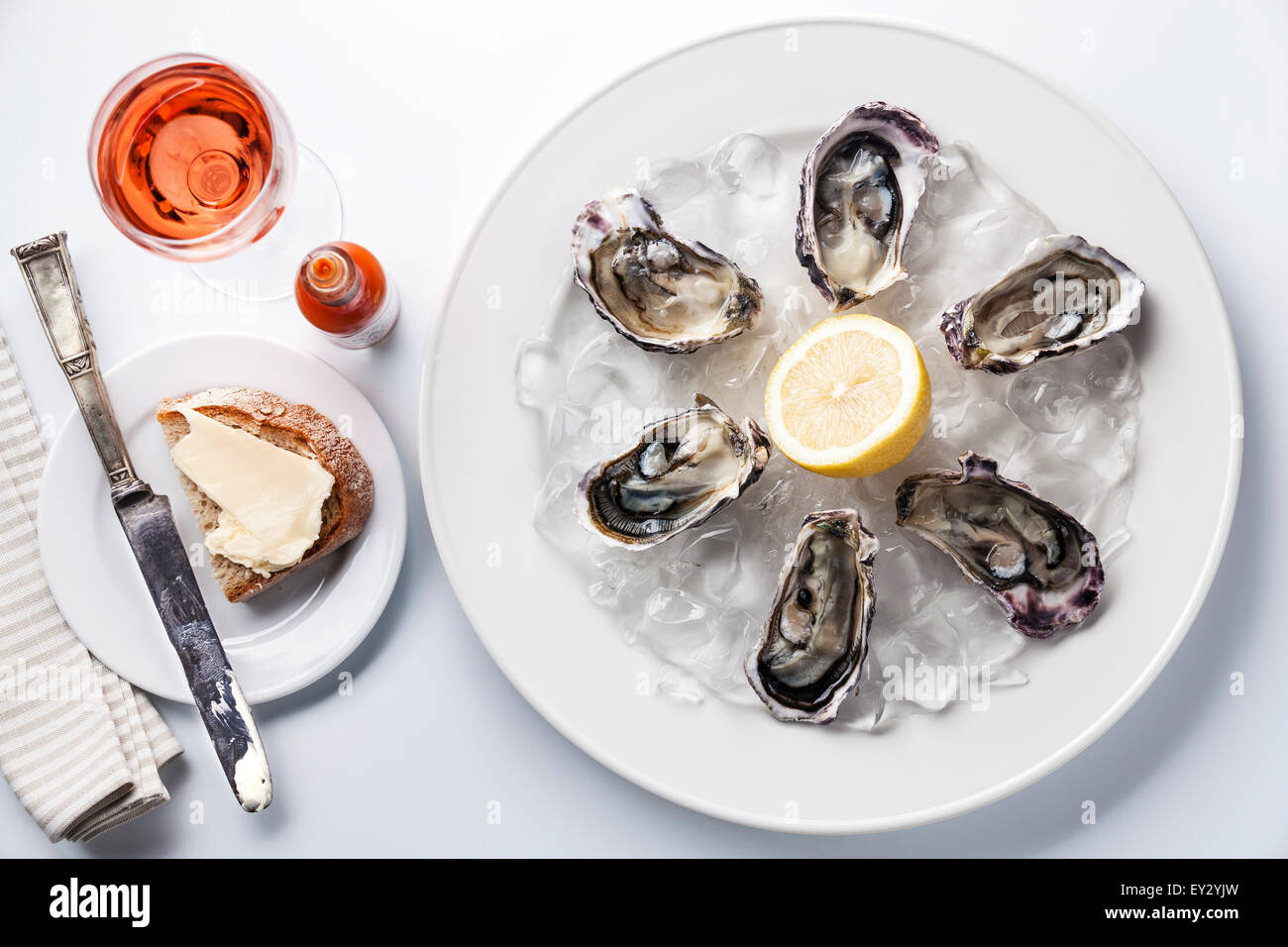 Opened Oysters on white plate, rose wine and dark bread with butter on white background Stock Photo