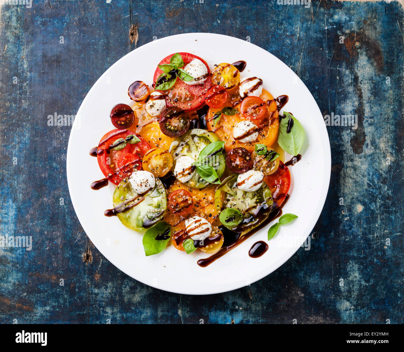 Colorful tomatoes salad with mozarella and balsamic vinegar on blue wooden background Stock Photo