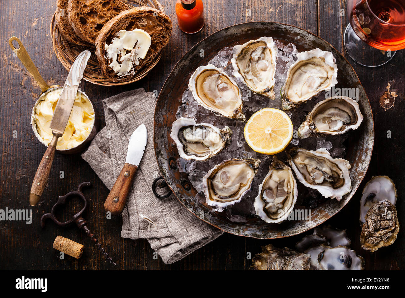 Opened Oysters on metal copper plate with dark bread with butter and rose wine on dark wooden background Stock Photo