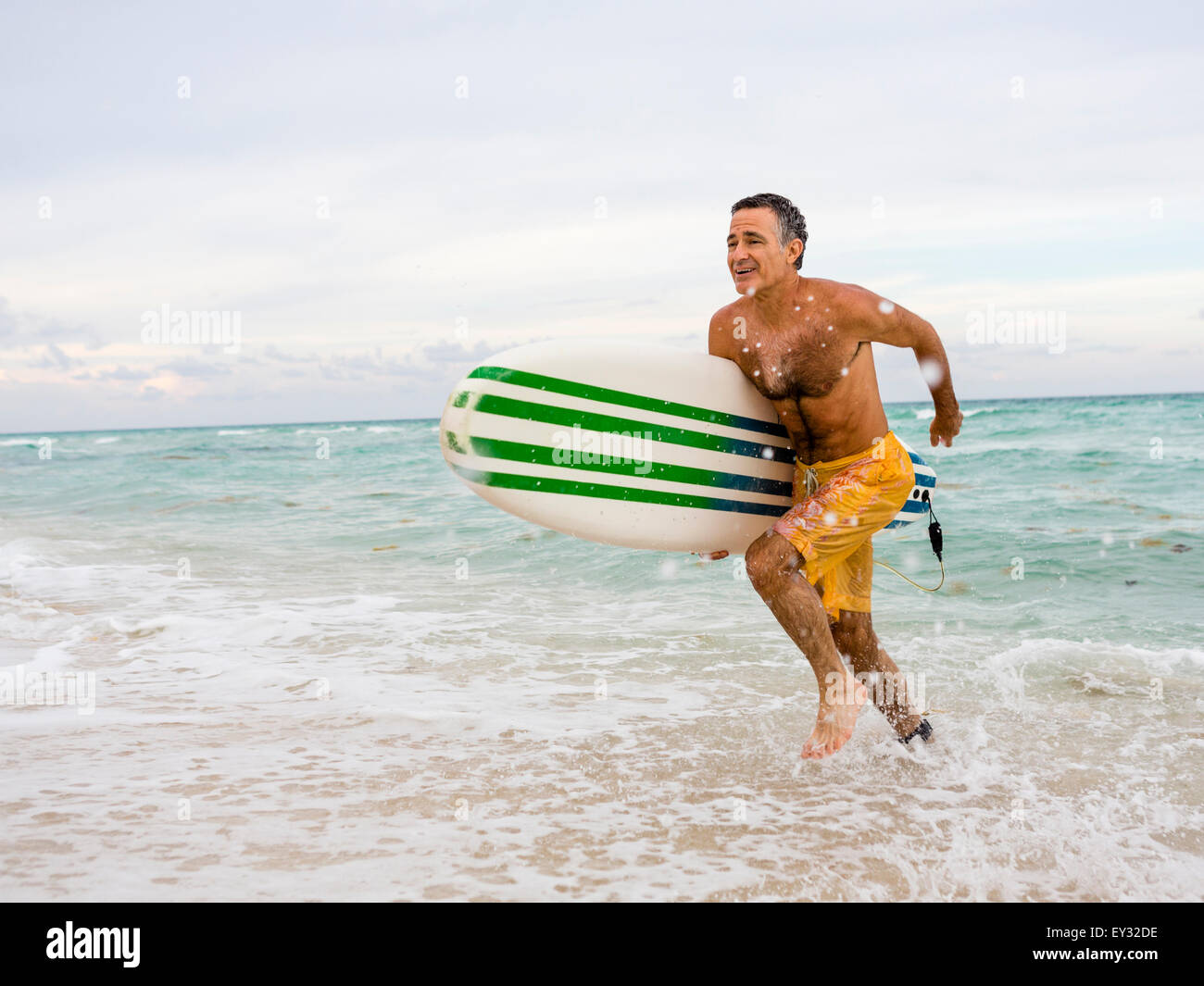 Senior man running quickly out of the surf holding a surfboard Stock Photo