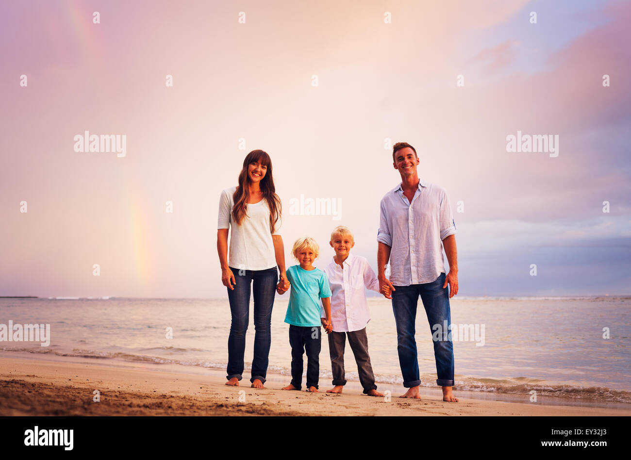 Happy young family on the beach at sunset with amazing rainbow Stock Photo