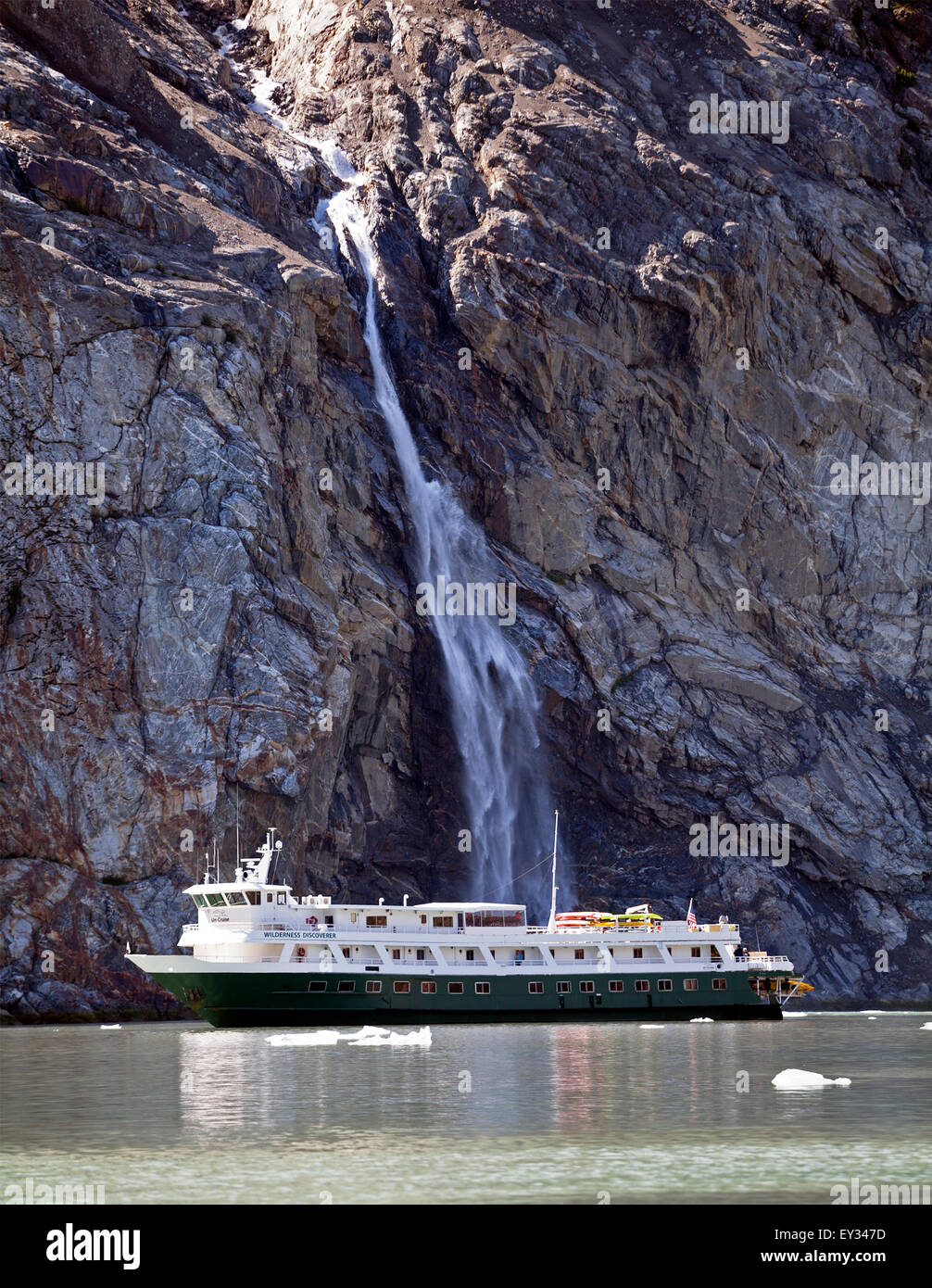 A cruise ship owned by UnCruise Adventures travels near a waterfall in the Inside Passage of Alaska between Juneau and Ketchikan. Stock Photo