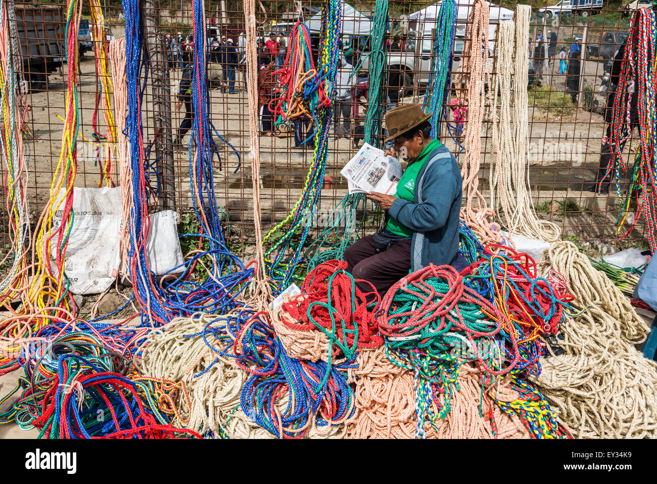 A man reading newspapers while selling colorful hand-made ropes at local market. Otavalo, Ecuador. Stock Photo