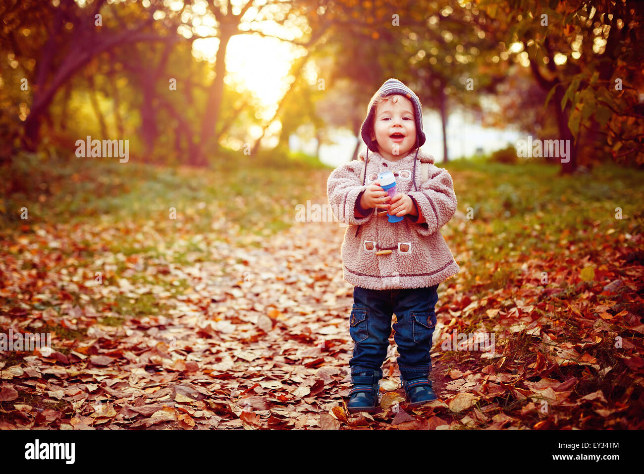 Funny Little 2 year old Kid Laughing and Walking in the Park at the Sunset with Toy in His Hand. Happy Childhood Concept. Stock Photo