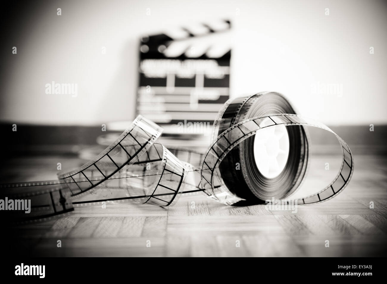 35 mm cinema film reel and out of focus movie clapper board in background  on wooden floor in vintage black and white Stock Photo - Alamy