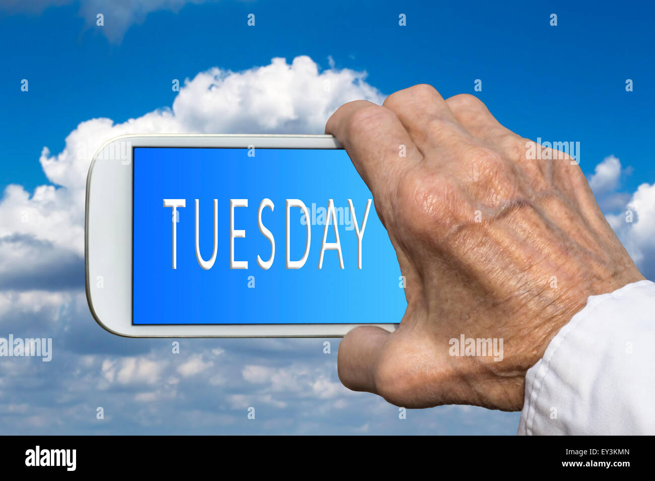 Smart phone in old hand with days of the week - Tuesday on screen. Selective focus. Stock Photo