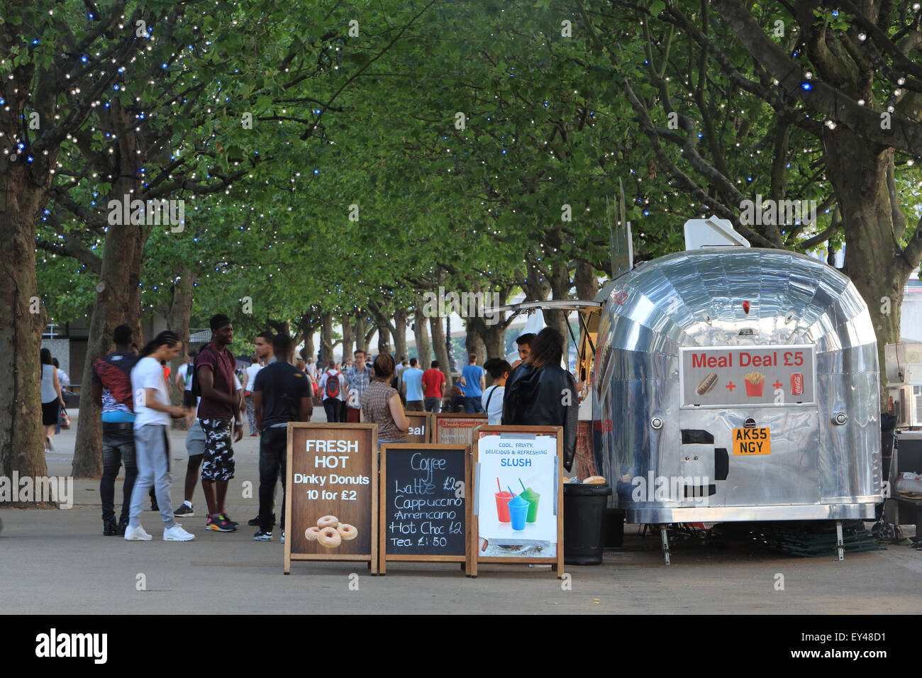 A busy, summer's evening on London's popular South Bank, with people strolling along the riverside avenue of trees, England, UK Stock Photo
