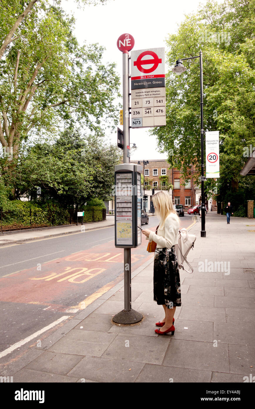 London bus stop; A woman waiting for a bus at a bus stop, Newington Green, Islington, London UK Stock Photo