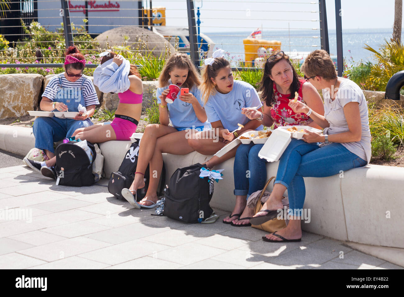 Group of females, women and teens, eating take away fish and chips at Bournemouth Pier Approach, Dorset UK outside Harry Ramsdens in July seaside Stock Photo
