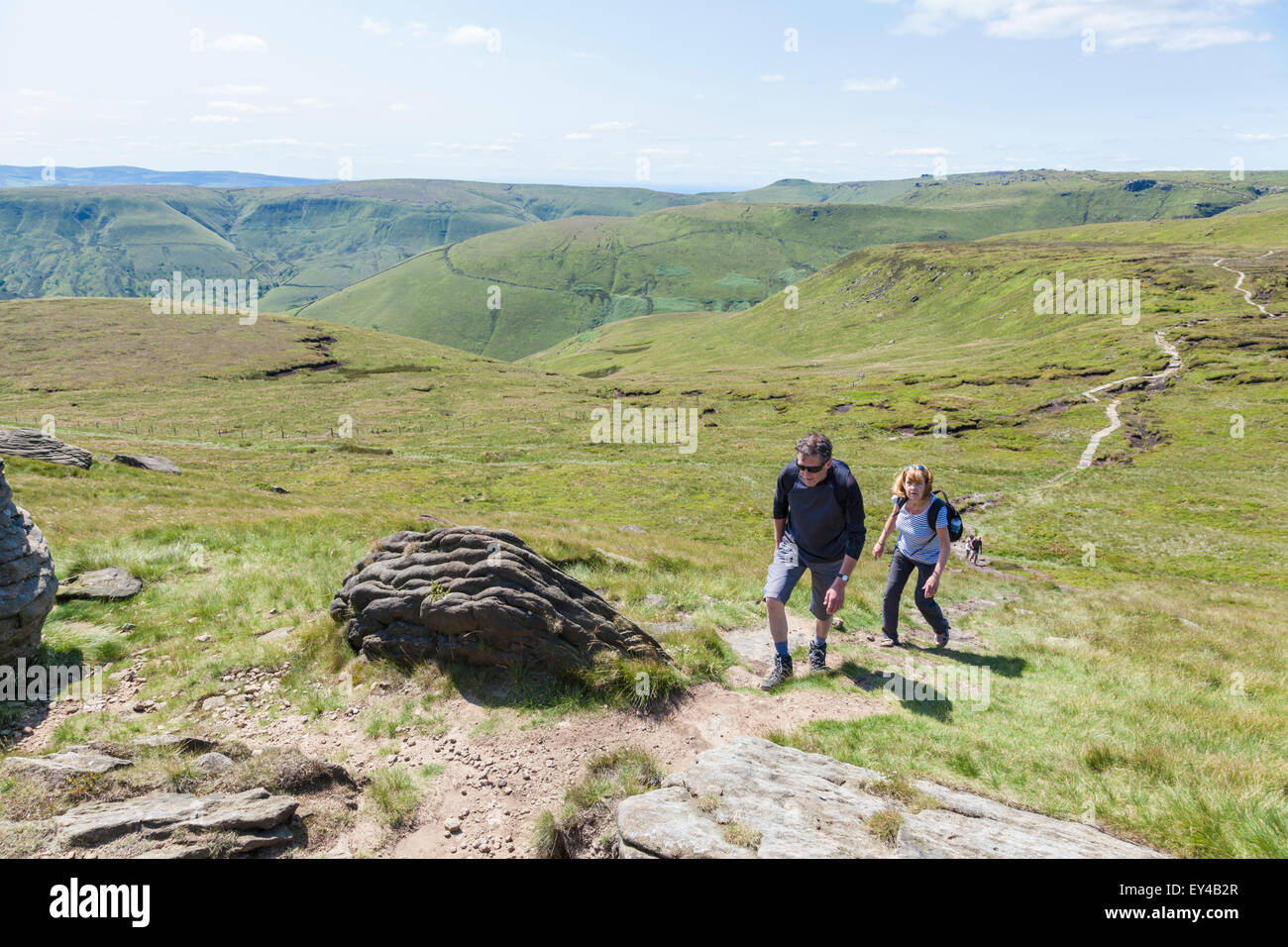 People hiking, UK countryside in Summer. Two hikers walking up the hill at Grindslow Knoll on Kinder Scout, Derbyshire, Peak District, England, UK Stock Photo