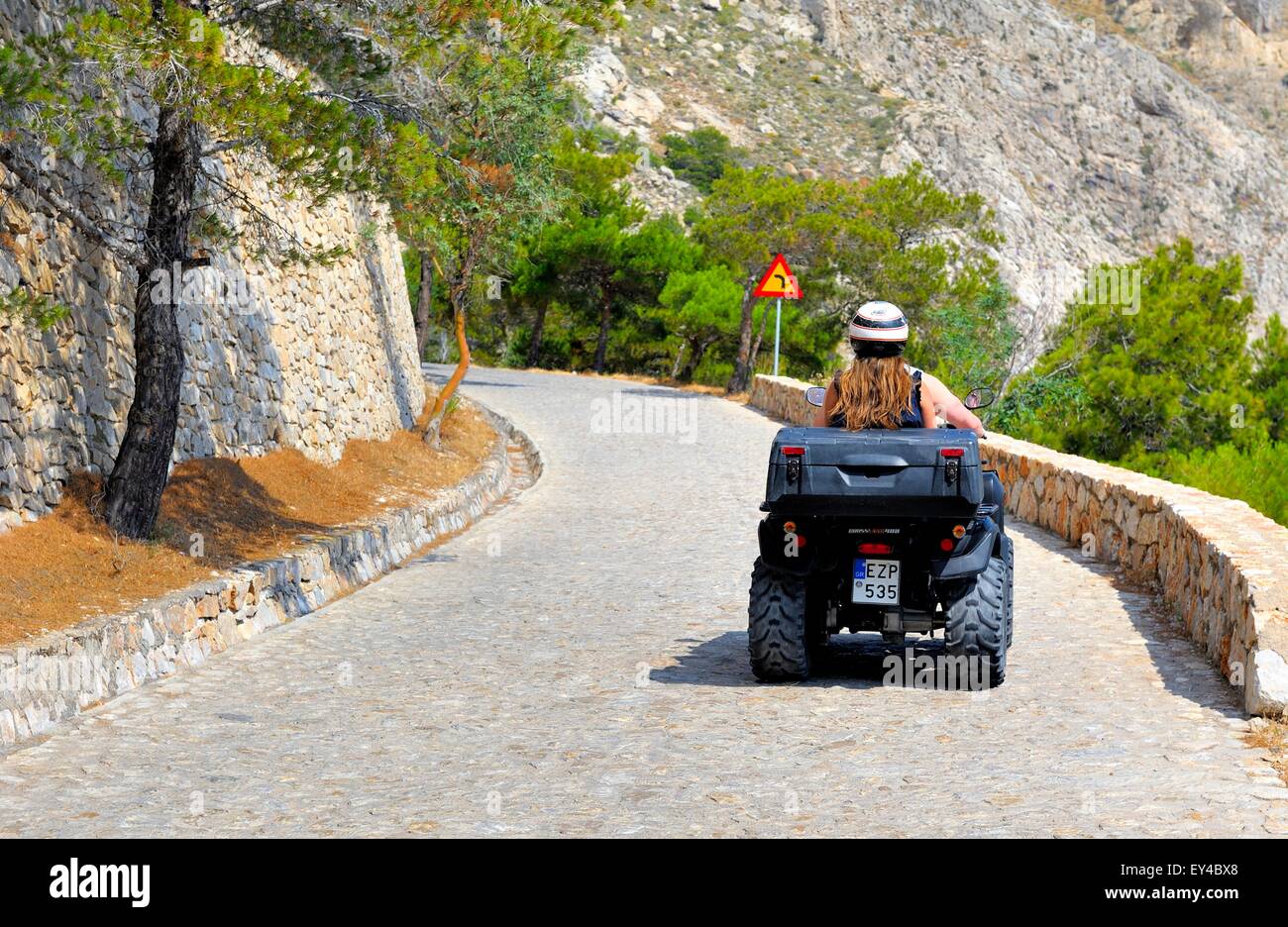 A young woman riding an ATV quad rental bike up the road to ancient