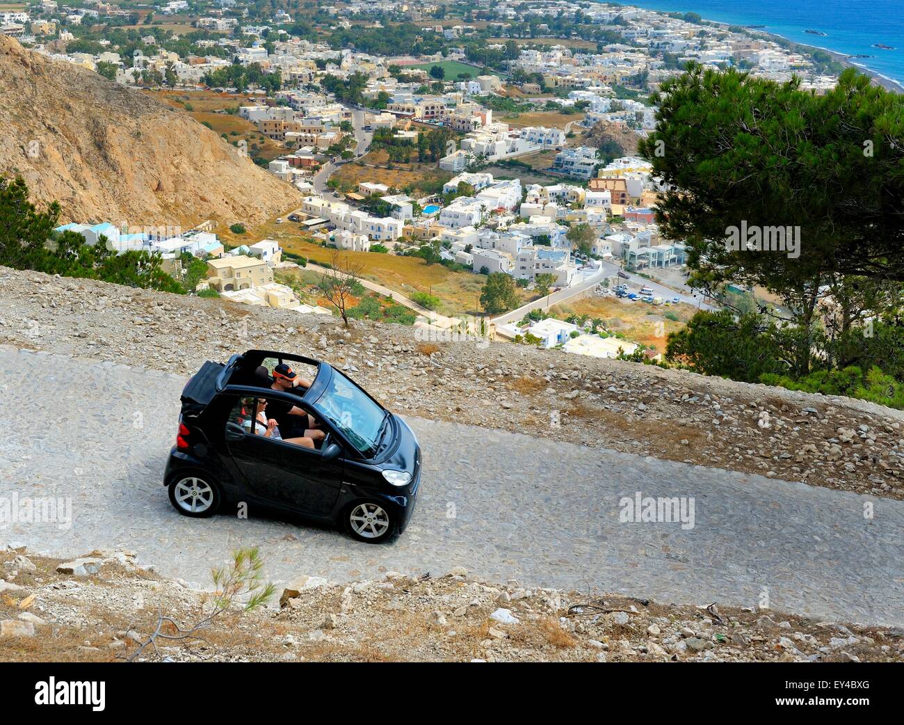 A black smartcar holiday hire vehicle on the winding road up to ancient Thira,Kamari,Santorini,Greece Stock Photo