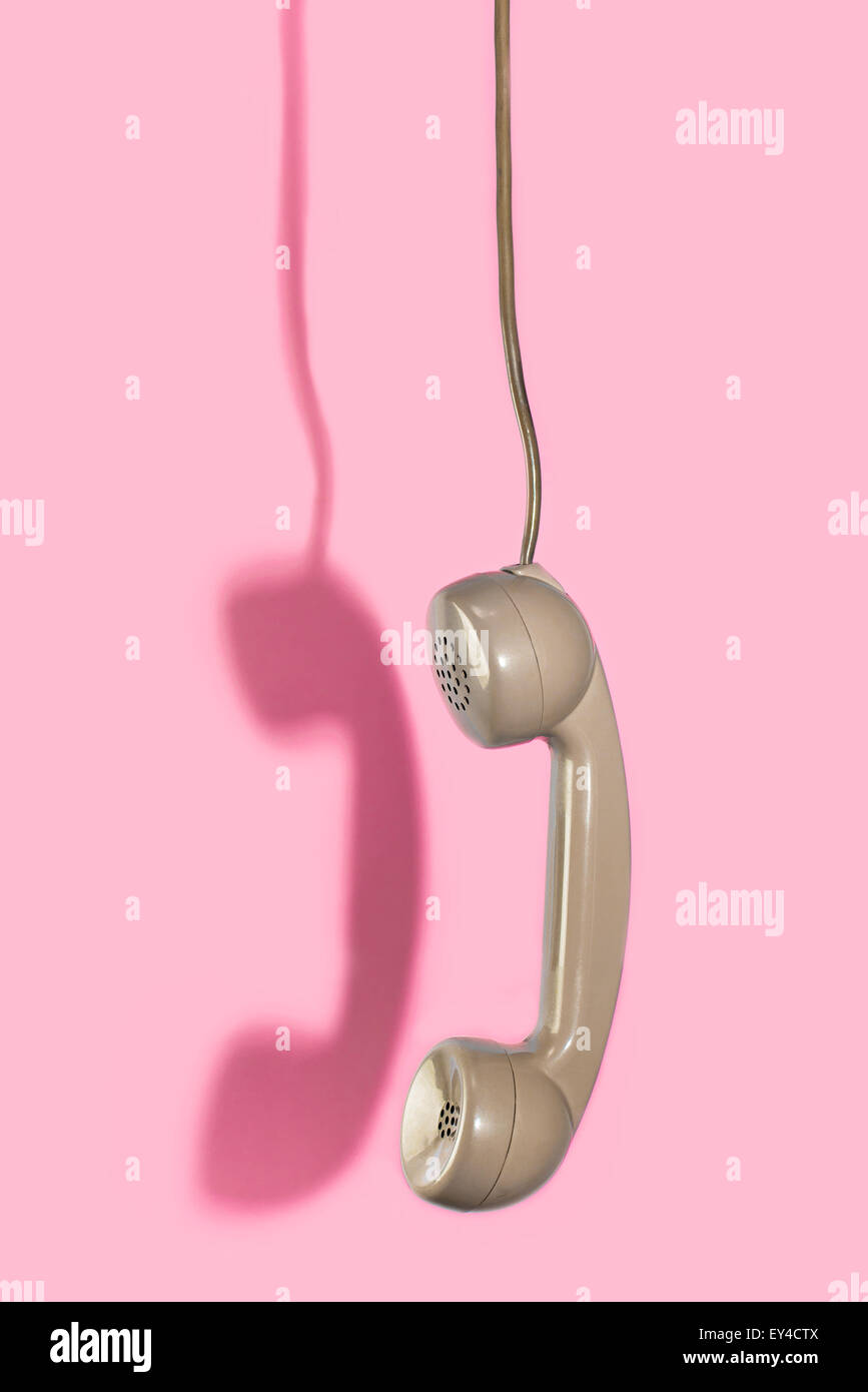 Vintage Green Telephone Receiver Hanging Upside Down Against Pink Background Stock Photo