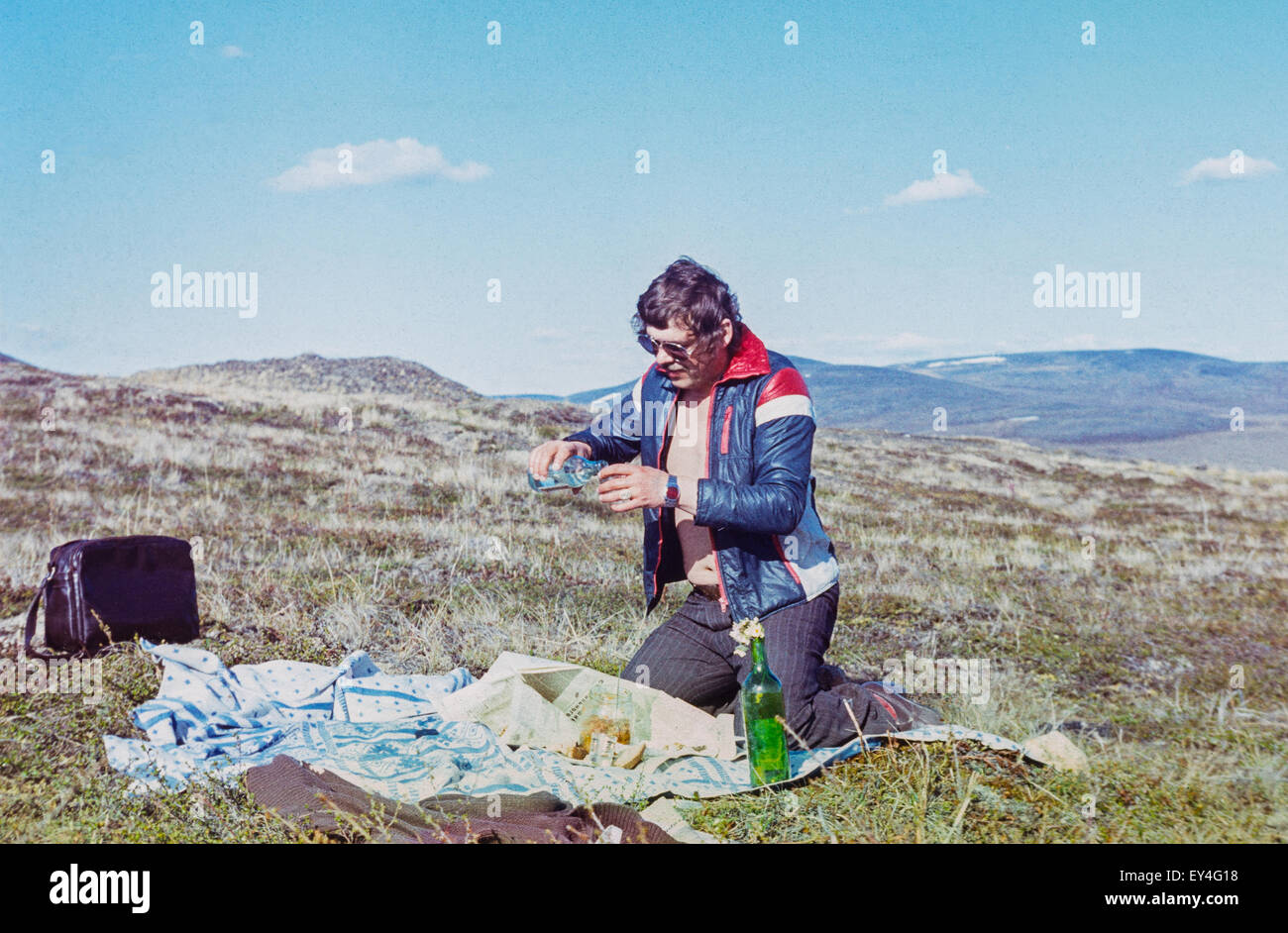 Young soviet gold-prospector fills jigger with russian vodka on outdoor picnic - Vintage photo taken in tundra Stock Photo