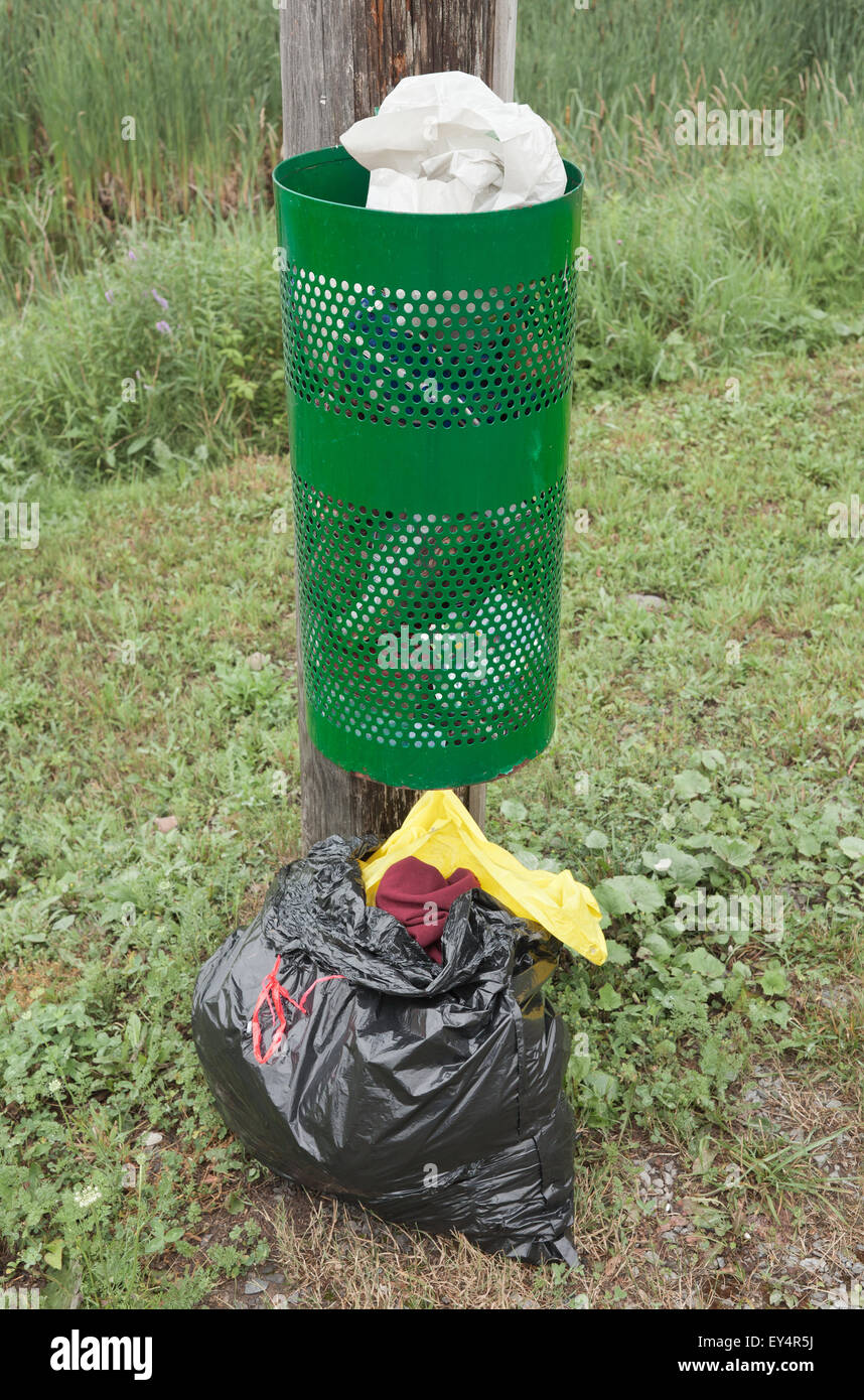 Green garbage bin on wooden pole with filled garbage bag on ground