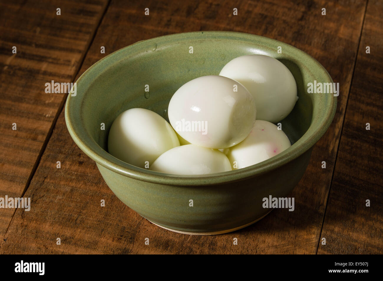 Green bowl on table with peeled hard boiled eggs Stock Photo