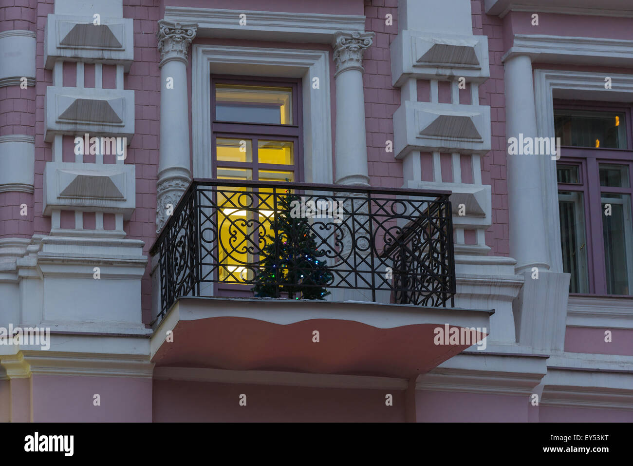 Artificial illuminated Christmas tree on a balcony of an old building. Illuminated window. Merry Christmas and Happy New Year Stock Photo