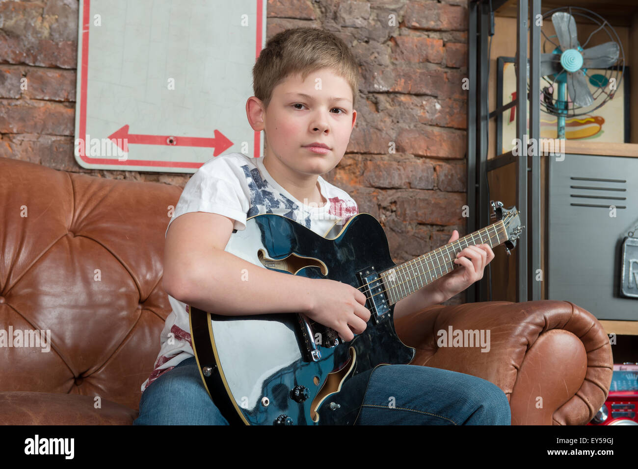 Male teenager sitting at home and playing guitar. Stock Photo