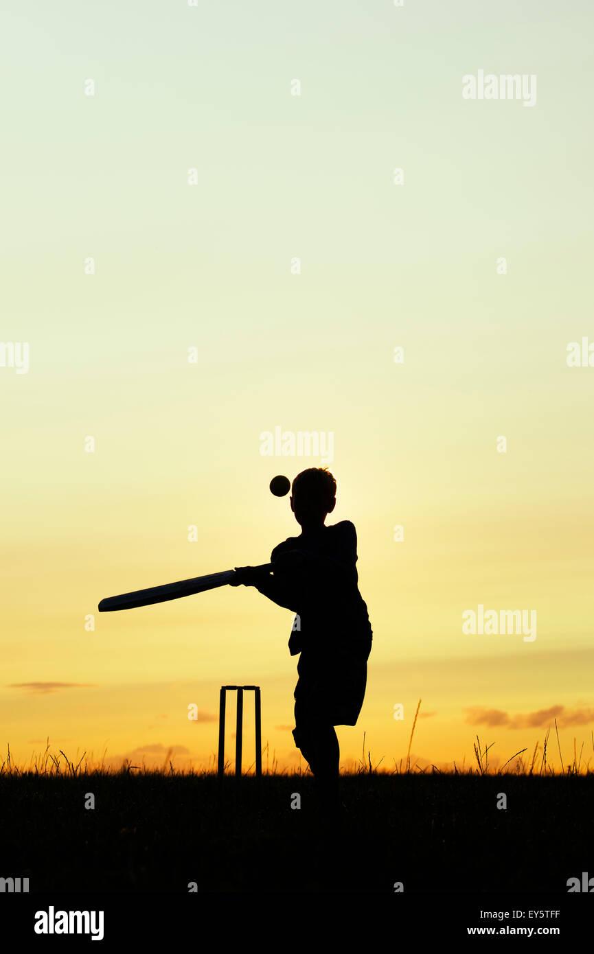 Silhouette of young boy playing cricket against a sunset background Stock Photo