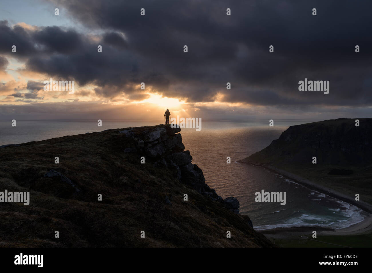 Female hiker watches midnight sun over sea from Nonstind mountain peak, Vestvågøy, Lofoten Islands, Norway Stock Photo