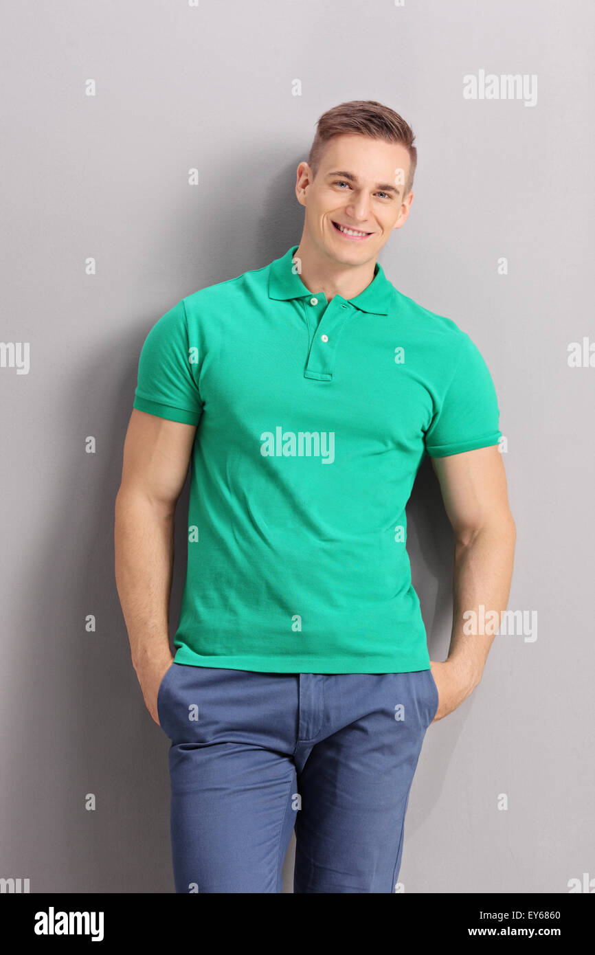 Vertical shot of a cheerful young man in casual clothes leaning against a gray wall Stock Photo