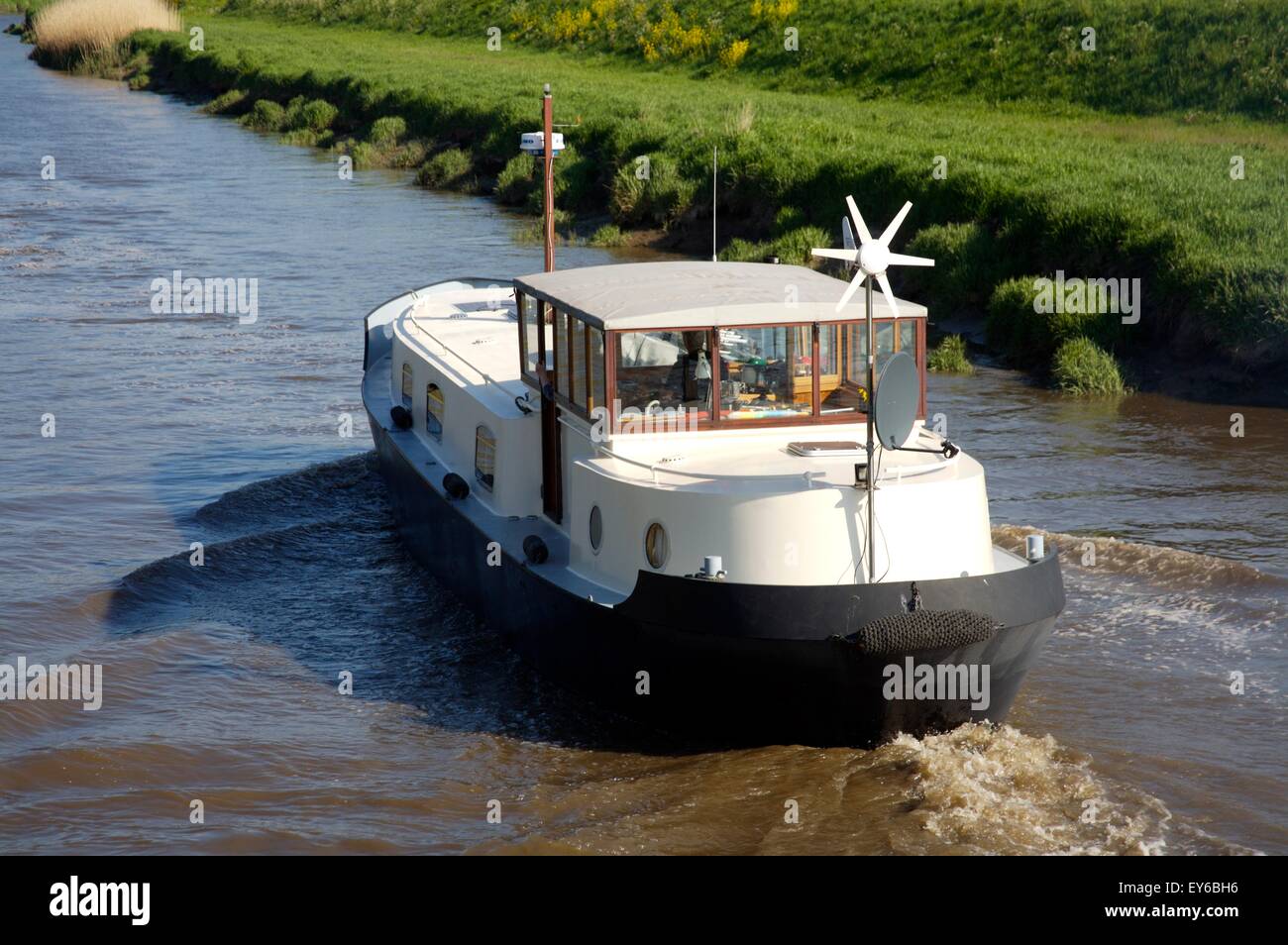 A Dutch barge (with a wind turbine) navigates down the River Douglas towards the Ribble Estuary, Lancashire, England. Stock Photo