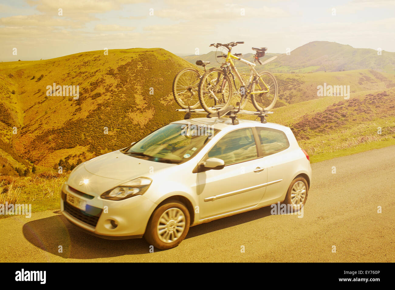 A moving car with two bicycles on the roof rack driving across the sunny Shropshire Hills in England, UK. Stock Photo
