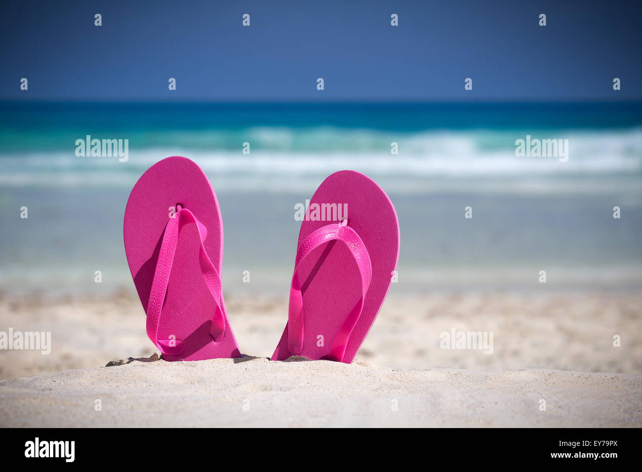 Pink flip flops on white sandy beach near sea waves, nobody. Summer vacation concept Stock Photo