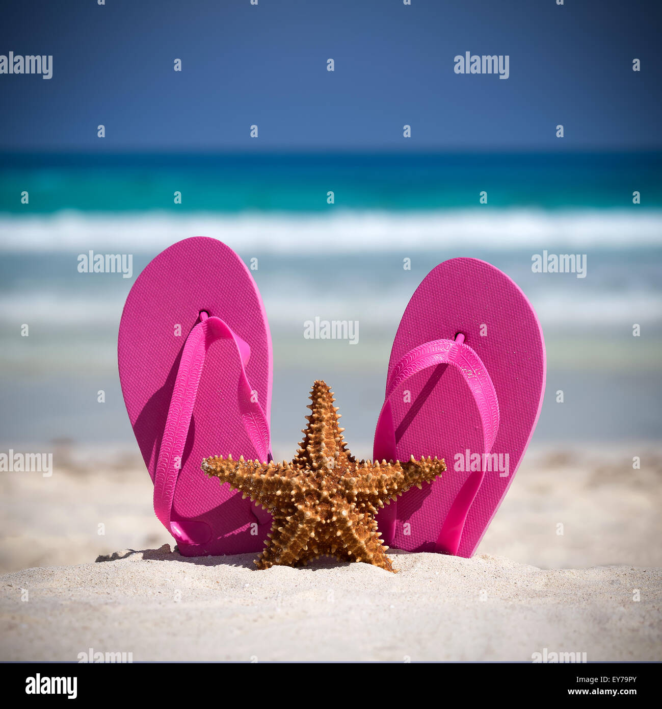 Pink flip flops and starfish on white sandy beach. Summer vacation concept Stock Photo