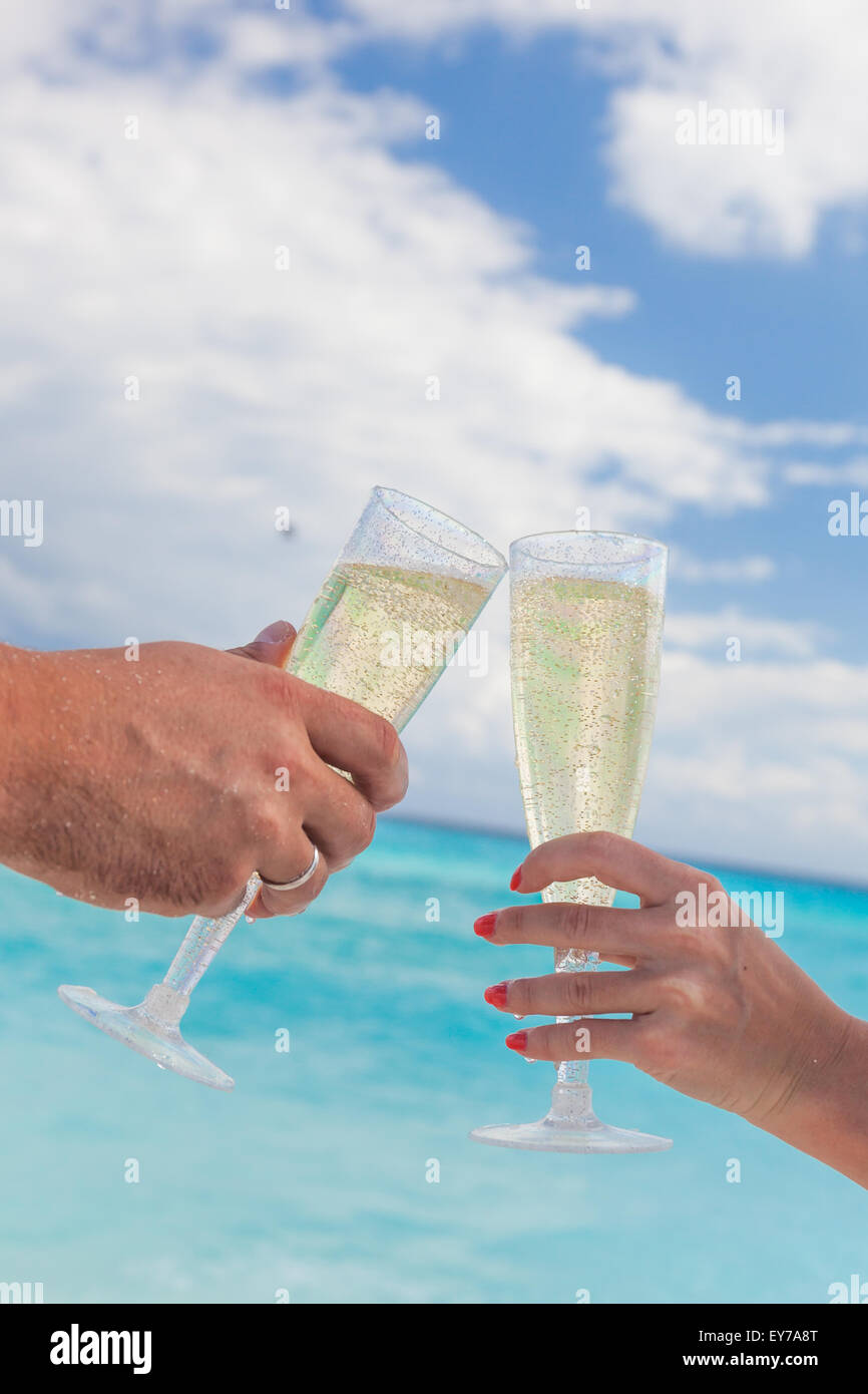 Clanging glasses with champagne at sandy beach and sea background ...