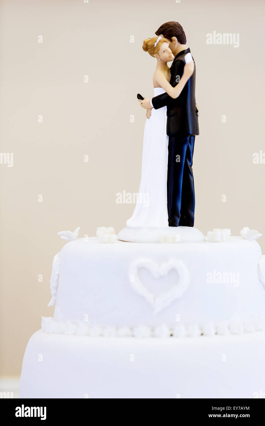 A wedding cake topper with bride and groom characters texting on mobile phones whilst at the same time hugging each other. An ironic comical scene Stock Photo