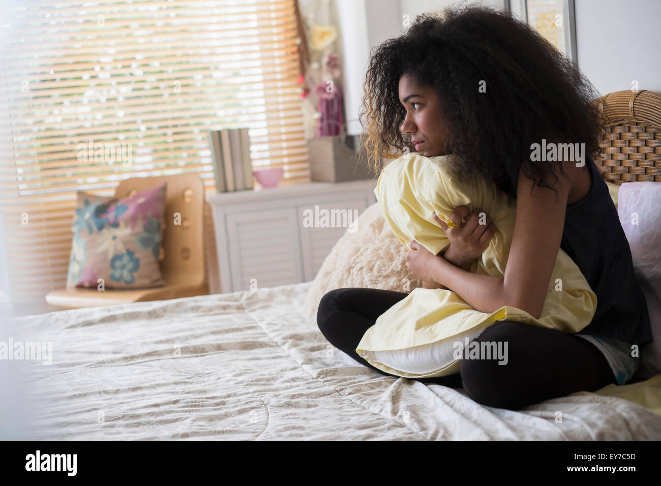 Teenage girl (14-15) sitting on bed, embracing pillow Stock Photo