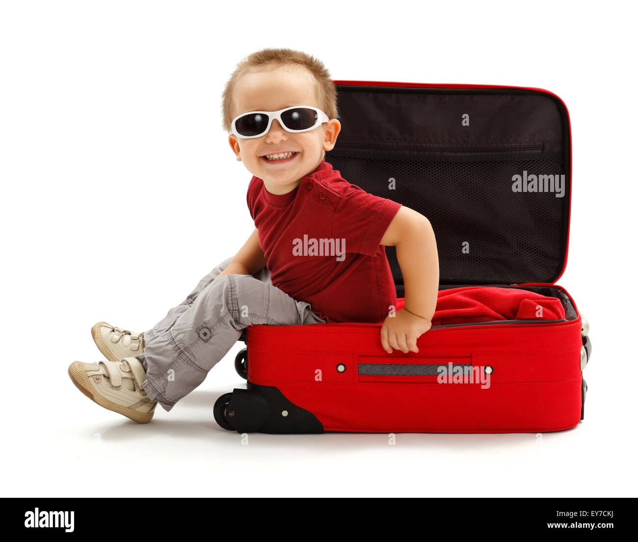Playful little boy wearing sunglasses, sitting in red suitcase Stock Photo