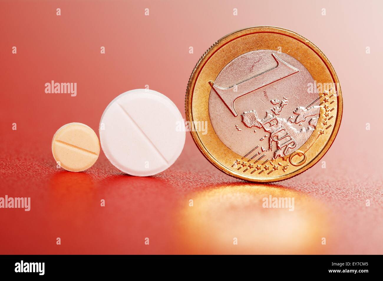 Two small pills standing beside one euro coin Stock Photo