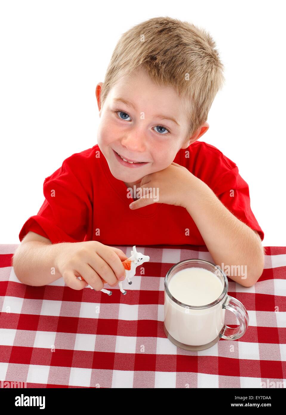 Cheerful young boy looking up, holding toy cow beside big glass cup of milk Stock Photo