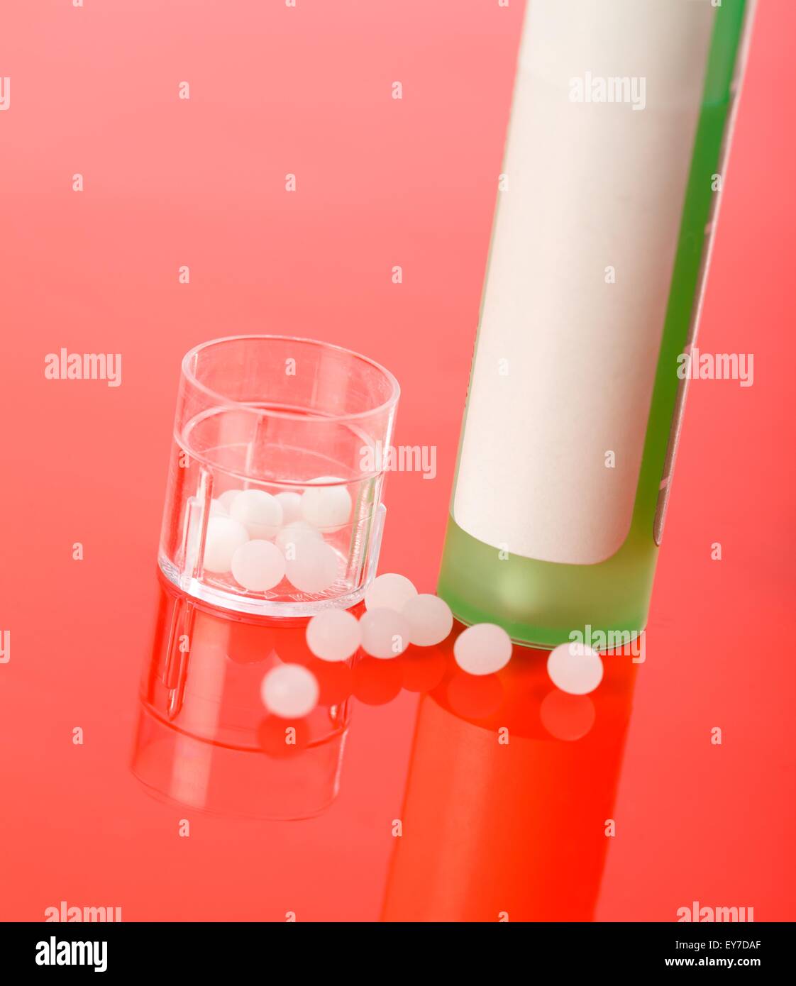 Homeopathic pills and container on reflective red background Stock Photo