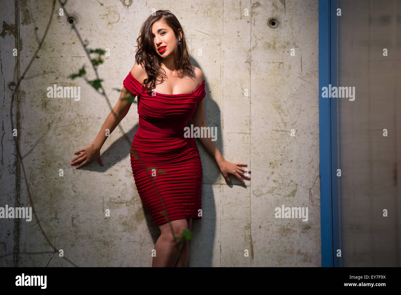 A sultry buxom full-figure brunette brown haired woman girl female model  wearing a figure hugging red dress posing in a fashion photography  photo-shoot on location UK Stock Photo - Alamy